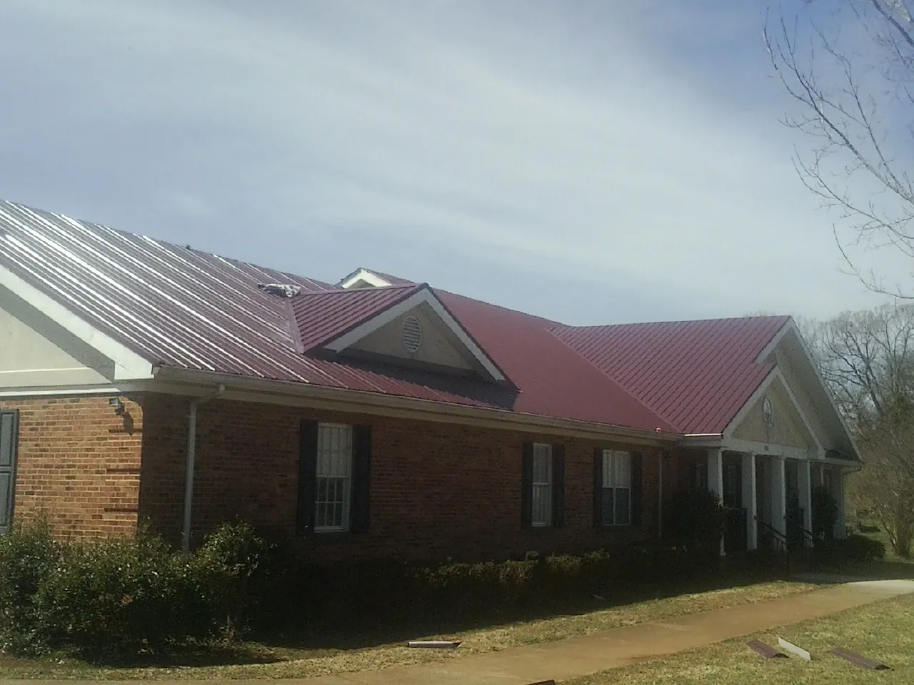 Red metal roof with gabled entries on a long brick building, from a Hail Damage Roof Repair job in Chelsea